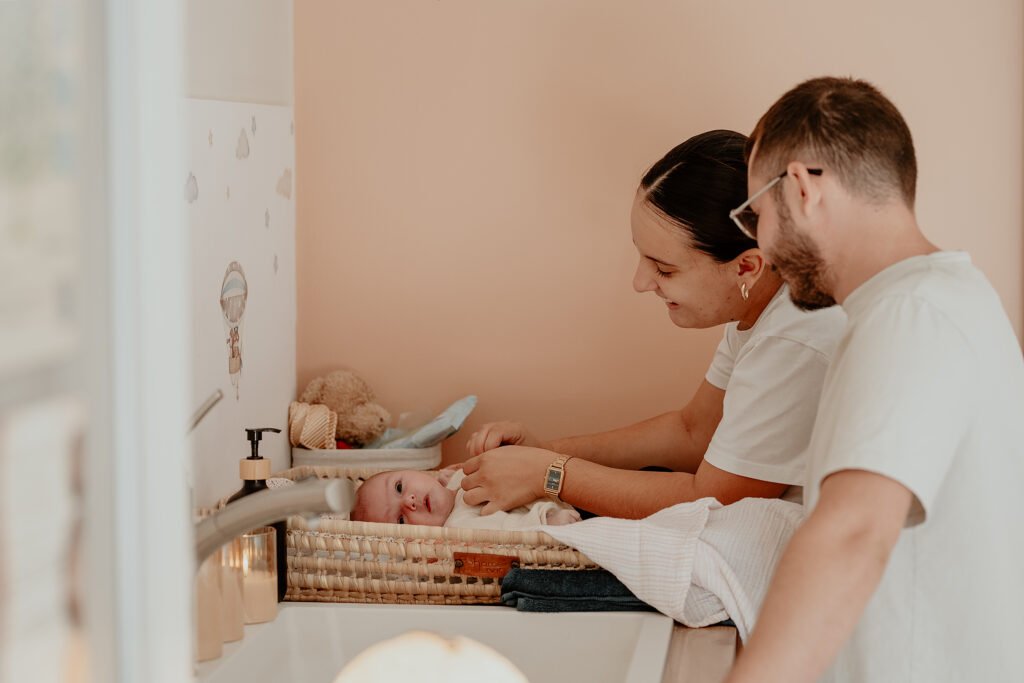 Parents souriants penchés sur leur nouveau-né allongé sur un plan à langer en osier après le bain thérapeutique