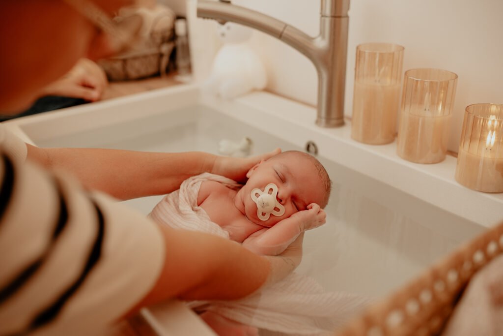 Nouveau-né endormi avec une tétine, emmailloté dans un lange rose dans l’eau du bain thérapeutique, à la lumière de bougies